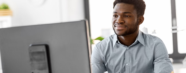 A young man smiles at a computer screen.